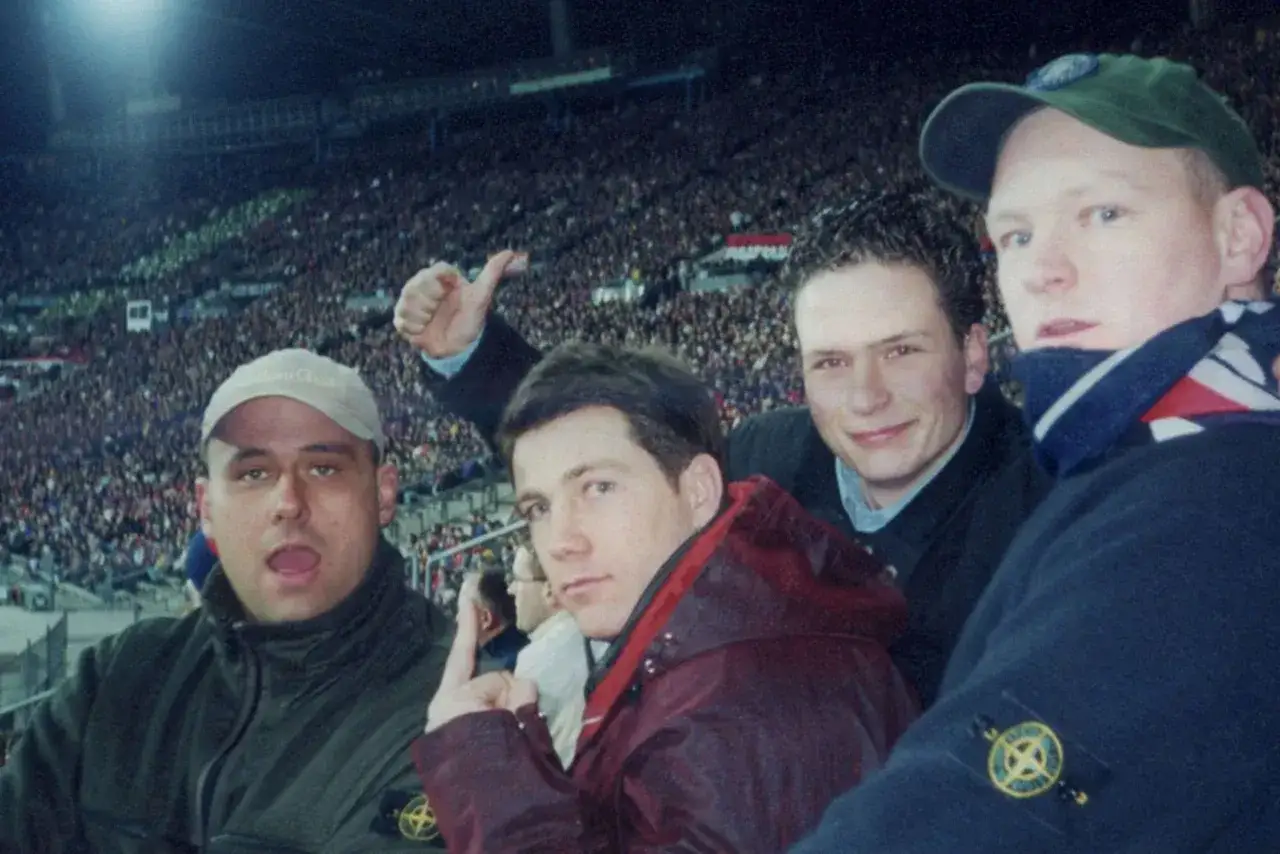Vier Freunde, die Stone Island tragen, jubeln bei einem Fußballspiel.