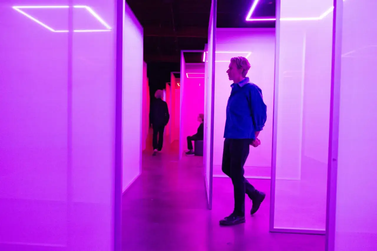 Menschen in einem Labyrinth aus Licht. Eine faszinierende Installation Art mit leuchtenden Neonlinien und violettem Schein.