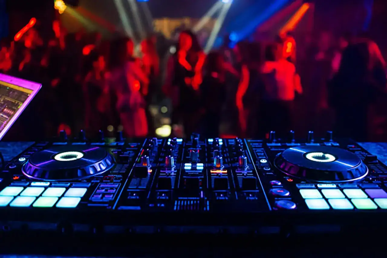 DJ-Pult mit leuchtenden Pads und Plattentellern, im Hintergrund eine tanzende Menge. Die Stimmung ist perfekt f&uuml;r eine Nacht mit algoriddim djay.