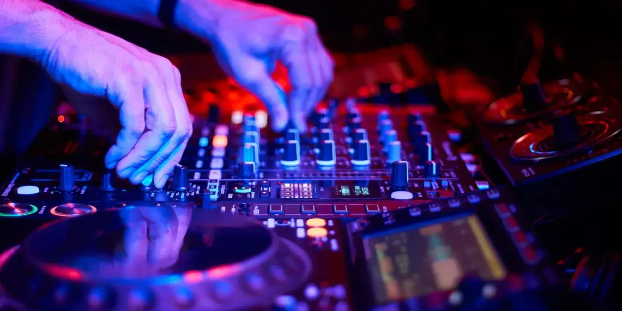 DJ-H&auml;nde am Mischpult, die den Beat f&uuml;r House Music kreieren, beleuchtet von blauem und rotem Licht.