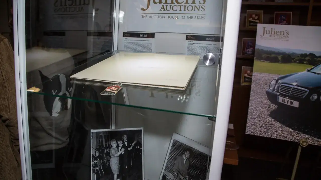 Die teuerste Schallplatte der Welt, Ringo Starrs UK 1st Mono Pressing White Album, wird in einer Vitrine ausgestellt. Daneben sind historische Fotos und ein Plakat mit einem Auto zu sehen.