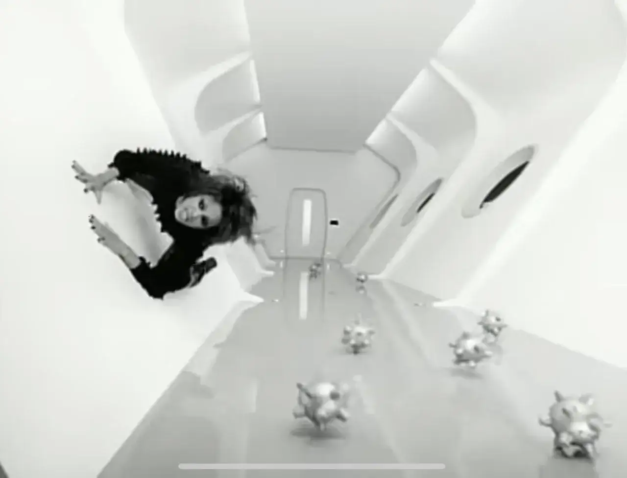 Eine Frau in Schwarz schwebt in einem futuristischen Gang, umgeben von kugelf&ouml;rmigen Objekten. Ein Szene aus dem teuerstes musikvideo aller zeiten.