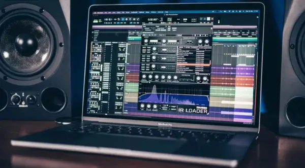 Ein MacBook Pro zeigt eine Musikproduktionssoftware mit einem IR Loader-Plugin, umgeben von Studio-Monitoren.